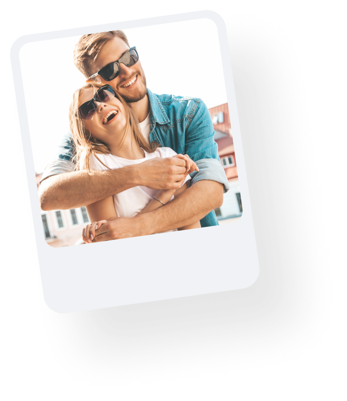 Man hugging woman from behind both wearing sunglasses on sunny day.