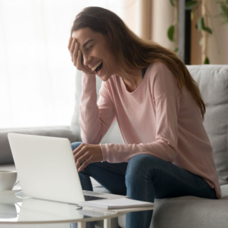 Laughing woman on computer with notepad next to her
