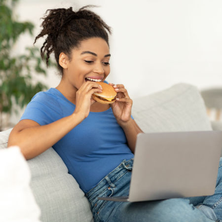 Woman eating hamburger while on video meeting