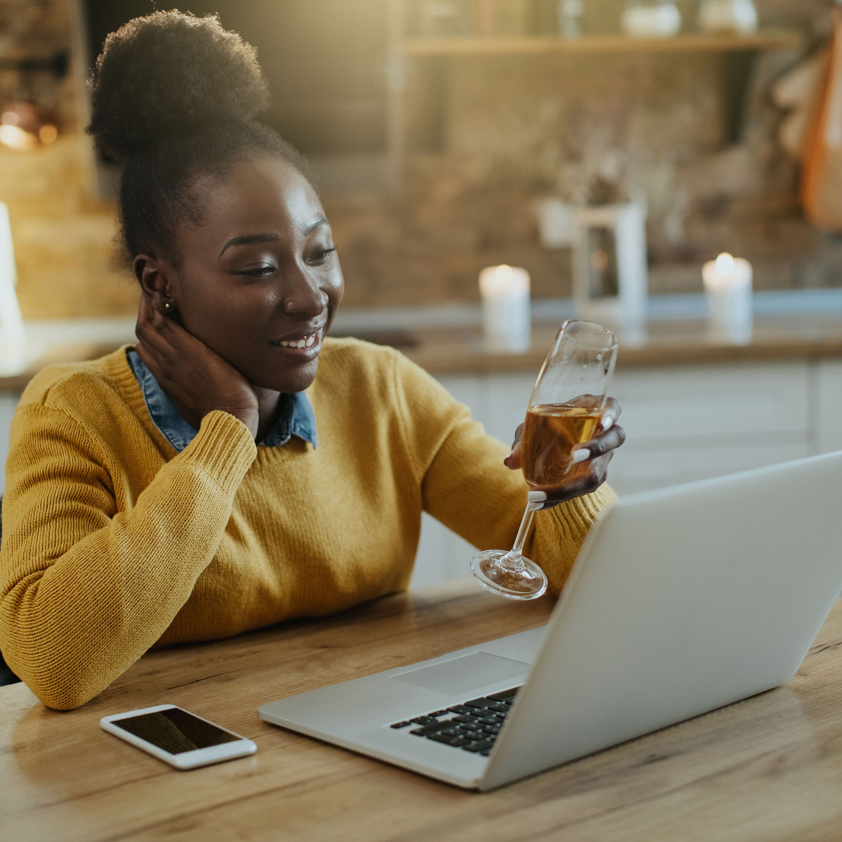 Woman sitting at computer while on an online speed date and toasting her date with a glass of champagne