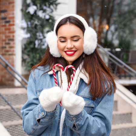 Smiling single woman holding two candy canes in a heart shape during the holiday season