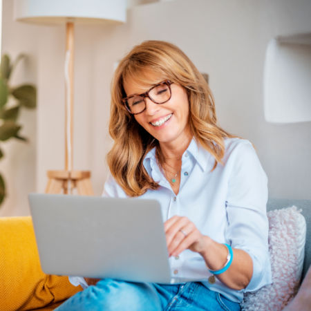 Woman in her late forties smiling while looking at her computer during an online speed date