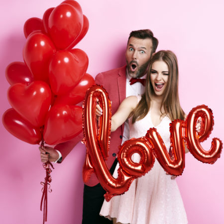 Singles (man and woman) at Valentine's Day party holding red heart balloons and a balloon that spells out "love"