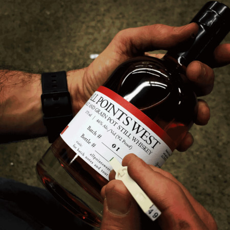 Hands holding bottle of whiskey made by All Points West Distillery