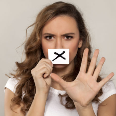 Woman holding an X in front of her mouth to signify avoiding talking about certain things on a first date