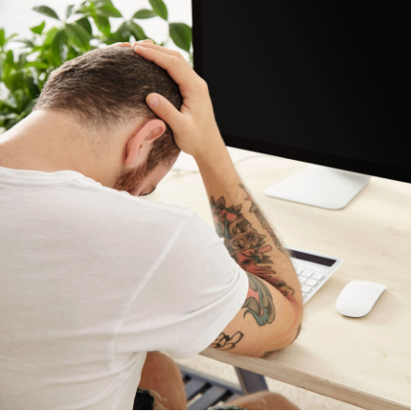 Man who used to catfish on dating apps sitting dejected in front of a computer with his head in hands