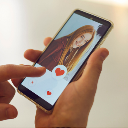 Hands of a catfisher holding phone as he looks at the dating app profile of a woman