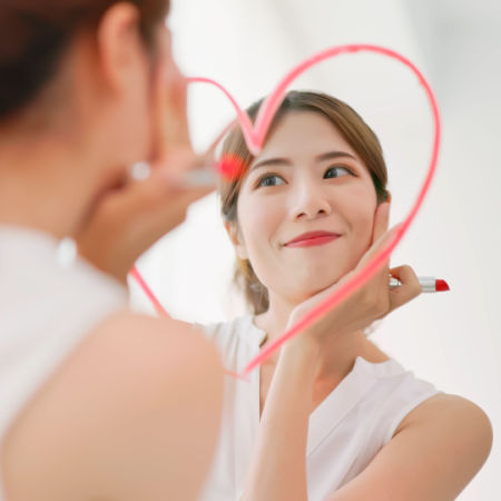 Single woman who lacks dating confidence stares at her reflection in mirror with lipstick heart drawn around her face