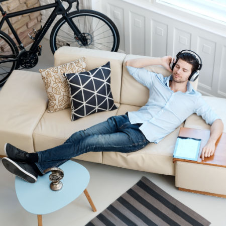 Single man enjoying life in his own apartment. He reclines on a couch, his bike in the background, as he listens to music.