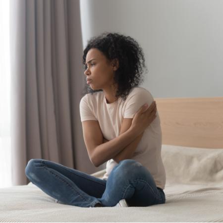 Stressed- and lonely-looking single woman, sitting on her bed alone.