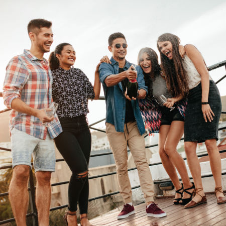 Group of happy single adults having fun on a deck and popping champagne
