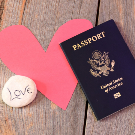 Photo depicting a long-distance relationship: a red heart overlaid with a U.S. passport and a stone with the word "love" written on it