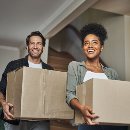 A man and woman formerly in a long-distance relationship carry boxes as they move in together