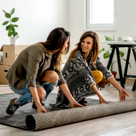 Formerly long-distant lesbian couple unrolls a rug in their new shared apartment