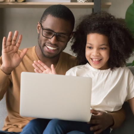 Single man sitting with daughter, introducing her to his new partner on a video call via computer