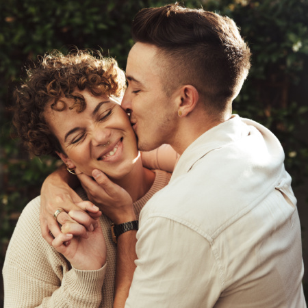 Man keeping the spark alive by giving his long-term partner a surprise kiss on the cheek as she smiles