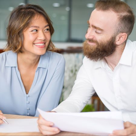 Coworkers (a woman and man) in a relationship sitting at a table and giving each other flirtatious looks.