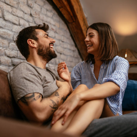 Laughing man and woman sitting together as they each wonder whether their casual relationship has the potential for something serious.