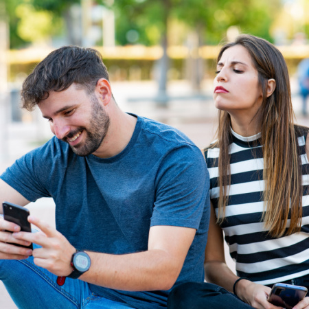 Man and woman in situationship. Woman looks over man's shoulder as he texts with another love interest.
