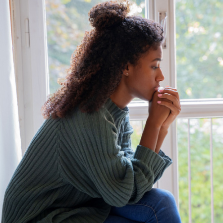 Somber woman sits in window after being betrayed