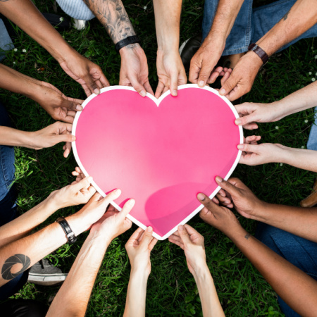 Image representing polyamory: many hands of different colors and sexes holding a pink heart