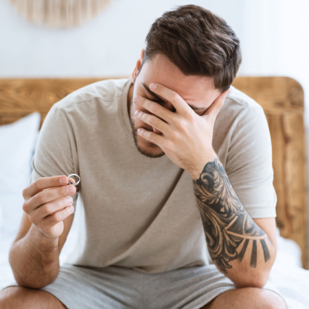 Man sitting on his bed holding his old wedding ring, looking worried about how his divorce and emotional baggage will affect dating