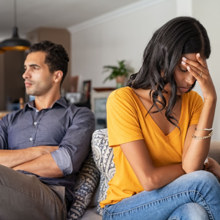 A couple -- man and woman -- are sitting on a couch looking distressed after having their first fight