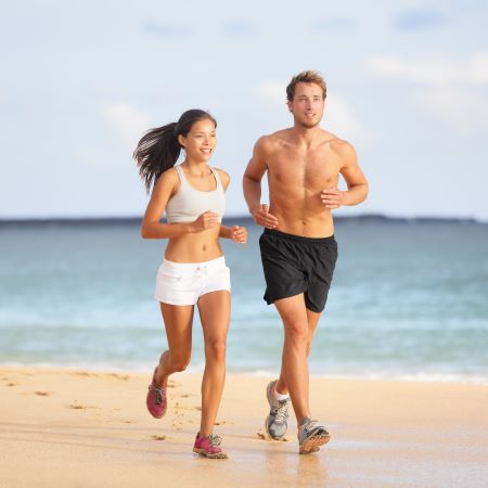 Fit couple (man and woman) running on the beach with the ocean in the background